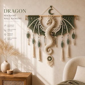 Puede incluir: Un tapiz de macramé que presenta una figura central de dragón de color crema con las alas extendidas, suspendido de una varilla de madera. El diseño incluye detalles en verde oscuro, borlas colgantes y una forma de media luna en la parte superior.