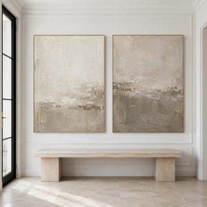 Pode incluir: Duas grandes peças de arte de parede retangulares com tinta impasto espessa e texturizada em tons neutros de bege, creme e taupe. As composições abstratas exibem traços horizontais em camadas e profundidade de superfície variada em molduras douradas finas.