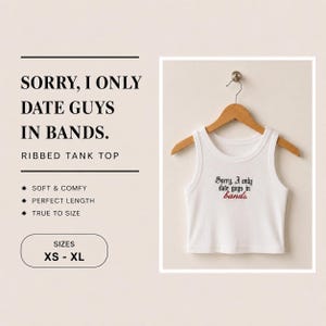 Może przedstawiać: Biały prążkowany podkoszulek wiszący na drewnianym wieszaku. Z przodu podkoszulka znajduje się wyhaftowany czarny napis "Sorry, I only date guys in", a słowo "bands." jest wyhaftowane na czerwono gotycką czcionką.