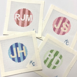 May include: Four square needlepoint canvases featuring circular designs with vertical stripes in pink, red, blue, and green. Each circle contains embroidered monogram letters RJM, JS, JH, and AB. Each canvas includes a small blue AC signature.