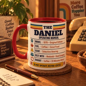 May include: A white ceramic mug with a red handle and rim, featuring the text THE DANIEL OPERATING MANUAL. It lists specifications including Model 1979, Fuel Coffee + Good Food, Issue Selective Hearing, Best With Weekends + Good Company, and Reboot Coffee + 20 Minutes Alone, ending with DO NOT OPERATE BEFORE COFFEE.