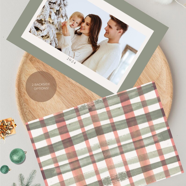 May include: Christmas card featuring a family photograph with the year 2024. The card has a sage green border and rests on a wooden tray. The reverse side displays a watercolour plaid pattern in red, green, and white.