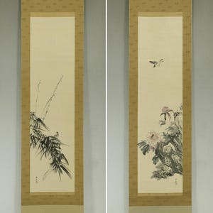 Peut inclure: Deux rouleaux suspendus japonais traditionnels. Le rouleau de gauche représente un oiseau perché sur une branche de bambou. Le rouleau de droite représente un oiseau en vol et des fleurs roses.