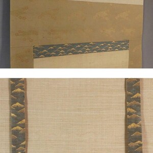 May include: A traditional Japanese scroll painting with a beige background and decorative bands. The bands feature a repeating pattern of gold and dark green mountain-like shapes. The scroll has a textured appearance and is designed to be hung.