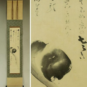 May include: A vertical Japanese hanging scroll featuring black ink calligraphy and a stylised ink wash painting of a dark, rounded form on a cream-coloured paper background. The scroll has a green patterned fabric border and wooden rollers.