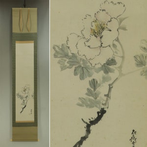 May include: A traditional Japanese hanging scroll painting depicting a white peony flower with green leaves and a black branch. The scroll is mounted on a green and gold fabric with a repeating pattern.