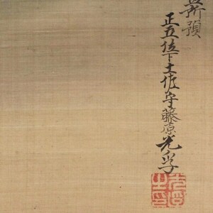 May include: Close-up of a beige-colored scroll with black calligraphy and a red seal. The calligraphy is vertical and includes Japanese characters. The seal is square and features intricate red markings.