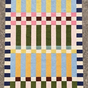 May include: A rectangular area rug featuring a geometric pattern of vertical stripes and horizontal bands. The design incorporates a palette of navy blue, cream, light blue, yellow, pink, dark brown, olive green, and soft teal in a grid layout.