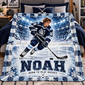 May include: A blue and white fleece blanket featuring a hockey player in a jersey with the number 18 and a wolf logo. The blanket displays the name NOAH and the text BORN TO PLAY HOCKEY, surrounded by snowflake patterns and a stadium background.