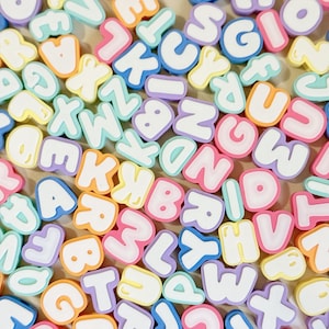 May include: A collection of colorful, chunky alphabet beads in various pastel shades including pink, blue, yellow, and purple. Each bead features a white letter on the front with a raised, rounded border, scattered in a random arrangement.