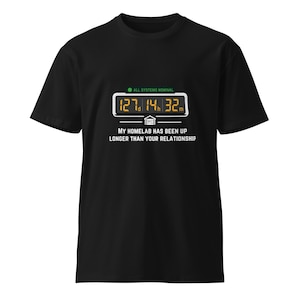 May include: A black t-shirt featuring a graphic of a digital timer displaying 127d 14h 32m, a green indicator light labeled ALL SYSTEMS NOMINAL, and the text MY HOMELAB HAS BEEN UP LONGER THAN YOUR RELATIONSHIP printed in white capital letters.