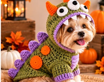 May include: A crochet pet sweater featuring a green dinosaur design with a hood, orange horns, white and black eyes, and white teeth. The back includes purple spikes and orange circular patches, with purple trim on the sleeves and hood edge.