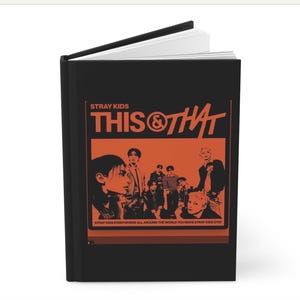 May include: A black hardcover book featuring an orange graphic on the front cover. The text reads STRAY KIDS THIS & THAT and STRAY KIDS EVERYWHERE ALL AROUND THE WORLD YOU MAKE STRAY KIDS STAY. The graphic includes a stylized illustration of a group.