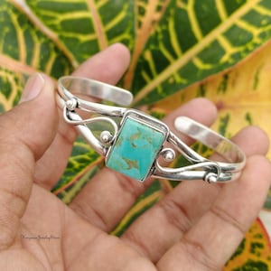 May include: A silver cuff bracelet featuring a rectangular turquoise stone with brown matrix patterns. The metal band has a polished finish and decorative wire detailing on both sides of the central stone setting. The piece is open-ended.