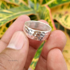 May include: A silver ring featuring a hammered, dimpled texture across the outer surface. The band has a polished finish and a consistent width, showcasing a reflective metallic appearance with small, circular indentations throughout the metal.