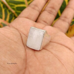 May include: A silver ring featuring a large, rectangular, milky white moonstone cabochon set in a smooth metal bezel. The stone has a flat top surface and a polished finish. The text Kingman Jewelry Store is visible in the bottom left corner.
