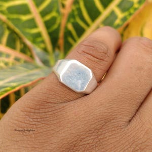 Op de afbeelding: Een zilveren zegelring met een glad, plat, zeshoekig vlak en een gepolijste metalen afwerking. De ring heeft een massief bandontwerp met strakke, hoekige randen. De tekst Kingman Jewelry Store is zichtbaar in de linkerbenedenhoek van de afbeelding.