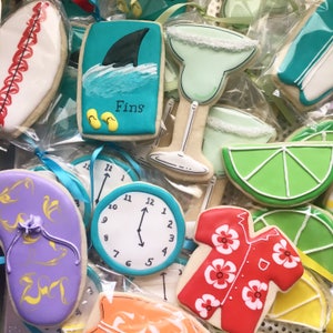 May include: A collection of decorated sugar cookies with various summer themes, including a shark fin, a margarita glass, a lime wedge, a clock, a flip-flop, and a Hawaiian shirt. The cookies are decorated with colorful icing and details.