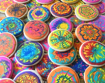 May include: A collection of colorful cookies decorated with swirling patterns in shades of blue, green, yellow, orange, and red. The cookies are arranged in a random pattern on a white surface.