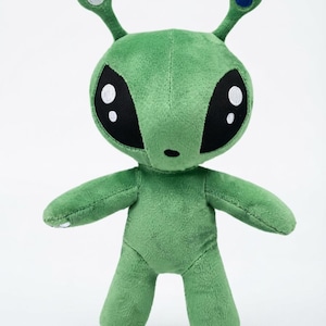 May include: A green plush alien toy with a large head, oversized black almond-shaped eyes featuring white highlights, and two antennae. The left antenna has a blue circular tip, while the right antenna has a silver circular tip.