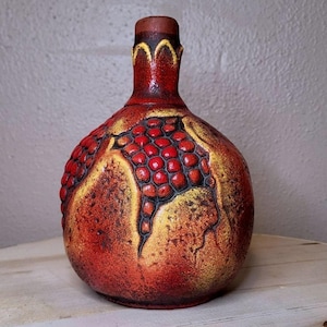 Pode incluir: Um vaso de cerâmica redondo com gargalo estreito, apresentando uma superfície texturizada com um gradiente de vermelho profundo e amarelo dourado. O corpo é decorado com segmentos vermelhos elevados e arredondados, contornados em preto.
