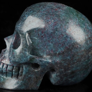 May include: A green and red gemstone skull sculpture. The skull is carved from a polished stone with a mottled green and red pattern.