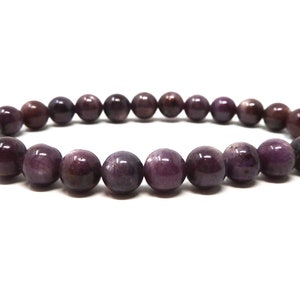Peut inclure: Un bracelet extensible composé de perles rondes et polies dans des tons de violet et de bordeaux. Les perles ont une finition lisse et brillante et sont enfilées sur un élastique. Le bracelet est présenté sur fond blanc.