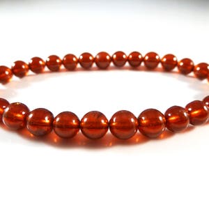 May include: A stretch bracelet featuring a strand of polished, round, amber-colored beads. The beads have a glossy finish and are strung together on an elastic band. The bracelet is displayed on a white surface.