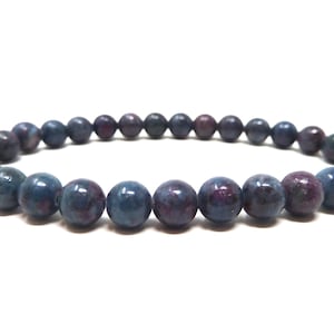 May include: A stretch bracelet composed of smooth, round beads in varying shades of deep blue, indigo, and dark purple. The beads feature a polished, glossy finish with natural mottled patterns and color variations throughout each individual stone.