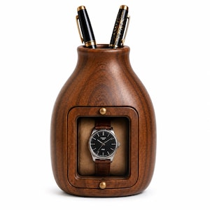 May include: A dark brown wooden desk organizer with a rounded, vase-like shape featuring a central rectangular display window containing a wristwatch with a black face and brown leather strap, and two black pens with gold accents in the top opening.