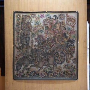 May include: A square painting on fabric featuring intricate, colorful illustrations of figures in traditional attire riding in a horse-drawn chariot. The artwork includes detailed floral motifs, ornate headpieces, and mythical creatures in muted earth tones.