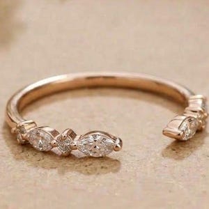 May include: A rose gold open ring featuring a series of marquise-cut and round-cut clear stones set along the band. The ring has an open design with the stones concentrated on the front section, creating a delicate and refined appearance.