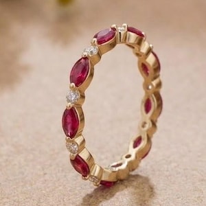 Puede incluir: Una alianza de oro con rubíes rojos de talla marquesa y pequeños diamantes blancos redondos alternados en un patrón circular continuo. El anillo tiene un acabado de metal pulido y muestra un contraste vibrante entre las piedras preciosas.