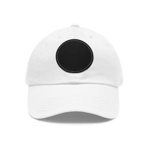 Può includere: Un cappellino da baseball bianco con una toppa circolare nera a tinta unita centrata sul pannello frontale. La toppa è fissata con cuciture bianche lungo il perimetro, in contrasto con il tessuto nero. Il cappellino ha una visiera curva.