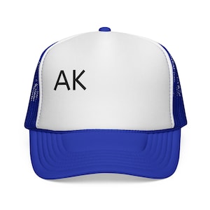 May include: A royal blue and white trucker hat featuring a solid white front panel with the black text AK printed on the left side. The cap includes a blue mesh back, a blue brim, and a blue button at the top center of the crown structure.