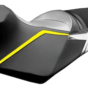 以下が含まれることがあります： 黒とグレーのマルチパネルデザインが特徴のオートバイ用シート。側面には鮮やかな黄色のアクセントストライプが施されています。後部には黒い背景に白い星のグラフィックパターンがあしらわれ、全体に輪郭に沿ったパッドが配置されています。