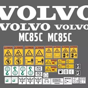May include: A collection of white and yellow adhesive decals on a grey background. The set includes large white VOLVO and MC85C text, along with various rectangular safety warning labels featuring black icons, text in Portuguese, and yellow borders.