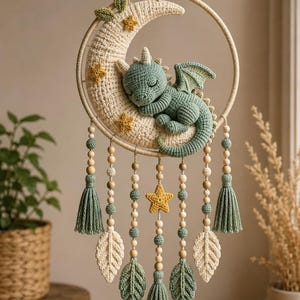 Può includere: Una decorazione da parete all'uncinetto con un cerchio, una luna crescente color crema e un drago verde addormentato. L'oggetto è decorato con piccole stelle gialle, perline di legno, nappe verdi e crema e ornamenti a forma di foglia.