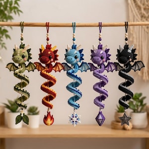 May include: Five hanging crochet dragon ornaments in green, red, blue, purple, and black. Each dragon features a long, spiraling tail, small wings, and a unique charm at the bottom: leaves, a flame, a snowflake, a diamond, and a star.