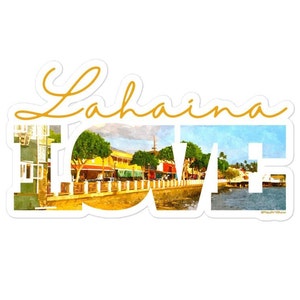 May include: A white sticker with the word "Lahaina" in a gold script font. The letters of "Lahaina" are filled with a watercolor image of a coastal town with buildings, trees, and water. The sticker has a white border.
