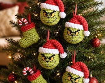 Könnte beinhalten: Eine Sammlung handgefertigter Häkelornamente, die an einem Weihnachtsbaum hängen. Das Set enthält drei runde, grüne Charakterköpfe mit rot-weißen Weihnachtsmannmützen sowie zwei grüne Häkelstrümpfe mit rot-weiß gestreiften Zuckerstangen.