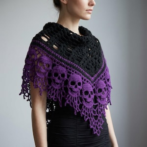 May include: A crochet shawl featuring a black upper section with a textured pattern and a vibrant purple lower section adorned with a repeating skull motif. The edges of the shawl are finished with an intricate, openwork fringe design.