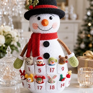 May include: A white crocheted snowman advent calendar featuring a black hat with holly, a red scarf, and two black buttons. The snowman has pockets labeled with numbers 1, 2, 5, 8, 9, 14, 17, and 18, each containing a small crocheted animal or figure.