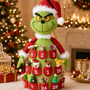 May include: A crochet advent calendar shaped like a green creature with a red Santa hat and white trim. The body features multiple red pockets, each labeled with a white number, containing small crocheted figures like bears, trees, and candy canes.