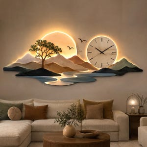 May include: A large wall-mounted decorative clock featuring a layered landscape design with mountains, a river, a tree, and birds. The piece includes a circular clock face with black hands and a warm, glowing backlight behind the mountain range.