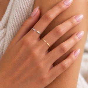 May include: Two open-style rings, one silver-toned and one gold-toned, each featuring a single letter engraved on the ends. The silver ring displays the letters O and K, while the gold ring displays the letters N and R. Both rings have a smooth finish.