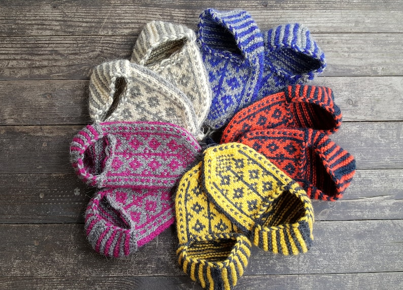 Puede incluir: Una colecci&oacute;n de cuatro pares de zapatillas de lana tejidas a mano dispuestas en un patr&oacute;n circular. Las zapatillas presentan intrincados patrones geom&eacute;tricos en combinaciones de colores contrastantes que incluyen amarillo y gris, rojo y negro, azul y gris, y crema y gris.