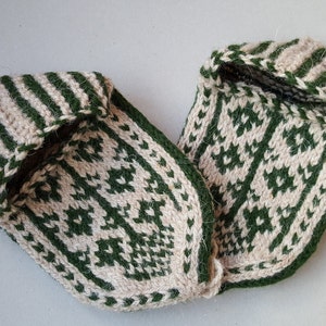 Puede incluir: Un par de zapatillas tejidas a mano con un esquema de color de dos tonos en verde bosque y crema. Las zapatillas muestran un patr&oacute;n geom&eacute;trico detallado en la parte superior y un dise&ntilde;o a rayas alrededor de la abertura del tobillo.