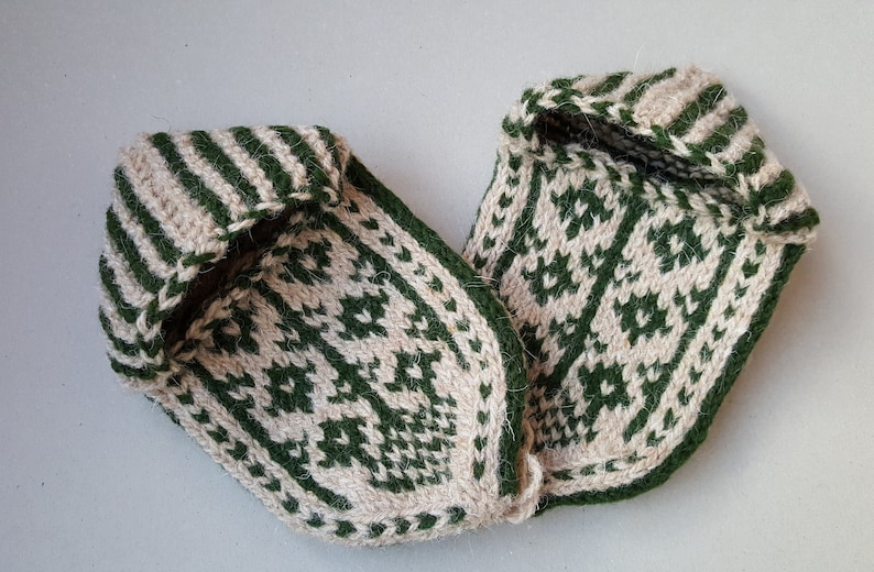 Puede incluir: Un par de zapatillas tejidas a mano con un esquema de color de dos tonos en verde bosque y crema. Las zapatillas muestran un patr&oacute;n geom&eacute;trico detallado en la parte superior y un dise&ntilde;o a rayas alrededor de la abertura del tobillo.