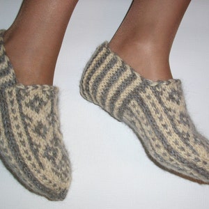 Puede incluir: Un par de zapatillas tejidas a mano con lana texturizada en tonos alternos de crema y gris carb&oacute;n. El dise&ntilde;o presenta un patr&oacute;n geom&eacute;trico de diamantes repetido en la parte superior y los lados, con detalles acanalados en el tal&oacute;n.